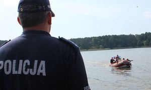 policjant, w tle łódż z ratownikami