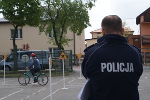 policjant stoi na terenie miasteczka ruchu drogowego i przygląda się uczestnikowi turnieju