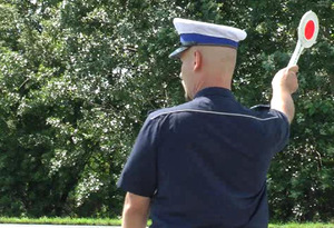 policjant trzyma wysoko w ręku tarczę dając znak do zatrzymania