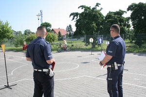 dwóch policjantów na placu i dziewczynka na rowerze