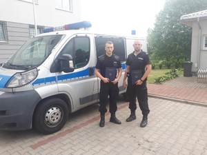 dwóch policjantów na tle radiowozu prezentują dyplomy