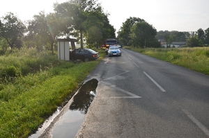 na drodze asfaltowej po lewej stronie wiata przystanku autobusowego, w której stoi na kołach pojazd