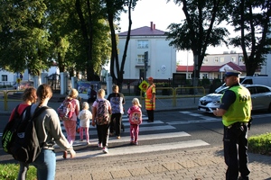 policjant patroluje rejon szkoły. W tle uczniowie z plecakami