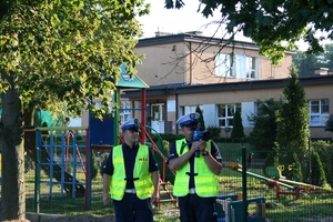 dwóch policjantów RD w rejonie szkoły. Jeden trzyma w ręku urządzenie do pomiaru prędkości