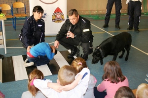 dziecko prezentuje pozycję żółwia. Policjanci kucają obok niego