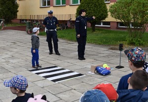 policjantka wspólnie z chłopcem stojąc przed matą przejścia dla pieszych rękami wskazują lewy kierunek