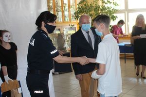 dyrektor i policjantka wręczają nagrody laureatowi konkursu