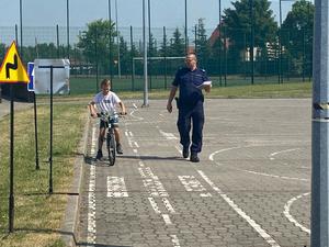 policjant z kartą egzaminacyjną, obok chłopiec na rowerze