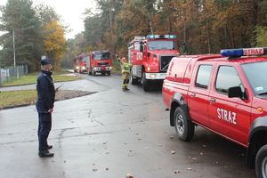 policjant przy wjeździe na zagrożony teren na szosie wozy strażackie