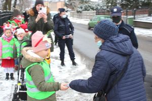 dziewczynka wręcza przechodzącej kobiecie opaskę odblaskową