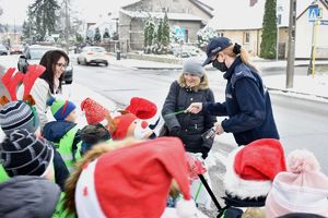 dzieci z policjantką wręczają przechodzącej kobiecie odblask