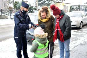 dziewczynka wręcza przechodzącym kobietom opaskę odblaskową