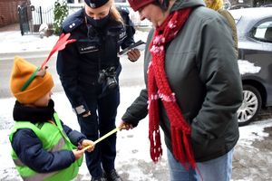 dziewczynka wręcza przechodzącej kobiecie opaskę odblaskową