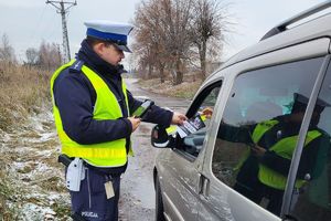 policjant wręcza kierowcy ulotkę i odblask