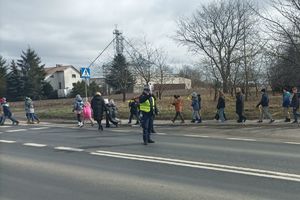 policjant czuwa nad bezpieczeństwem przekraczających jezdnię dzieci