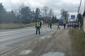 policjant czuwa nad bezpieczeństwem przekraczających jezdnię dzieci