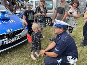 Dziecko puszczające bańki. Policjant klęczy obok dziecka.