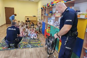 policjant rozmawia z dziećmi obok policjant z psem