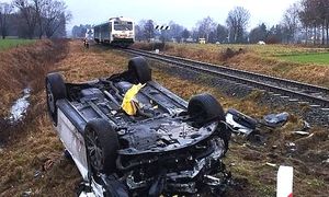 auto po kolizji leżące na dachu, w tle pociąg na torach