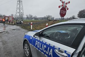 auto po kolizji leżące na dachu, w tle pociąg na torach, na pierwszym planie radiowóz