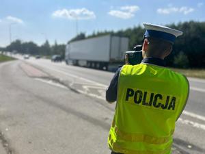 Policjant stoi na drodze i mierzy prędkość.