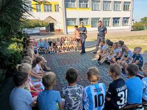 Policjanci stoją przed grupą dzieci, które siedzą na ławkach