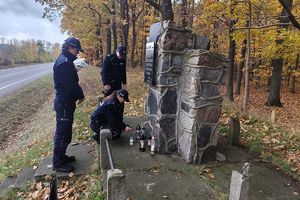 policjanci stawiają znicz przy obelisku