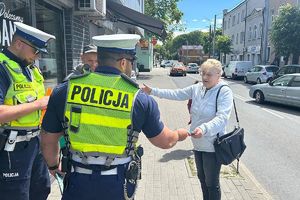 policjanci wręczają kobiecie ulotkę informacyjną