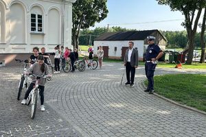 dyrektor szkoły z policjantem obserwują uczennicę na rowerze zdającą egzamin