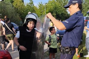 policjant pomaga chłopcu założyć strój szturmowy