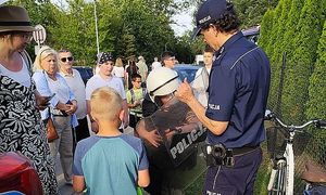 policjant pomaga chłopcu założyć strój szturmowy