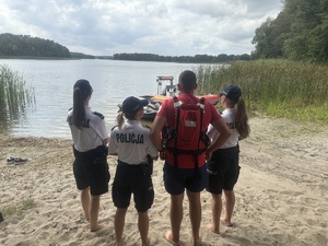 Policjanci i ratownik WOPR na tle jeziora