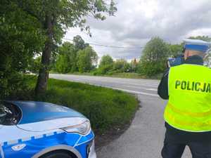 Policjant w żółtej kamizelce mierzy prędkość. Widać radiowóz