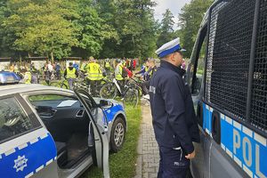 Policjant przy radiowozie. W tle uczestnicy rajdu.