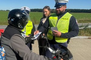 Policjanci i przedstawicielka PZU rozmawiają z kierowcą motocykla i wręczają materiały edukacyjne kampanii Mistrzu zwolnij