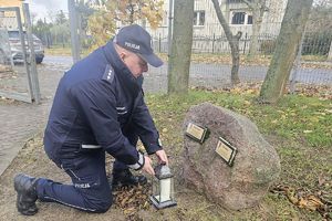 policjant ustawia znicz przy pamiątkowym kamieniu