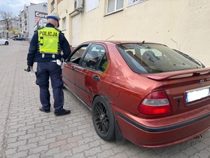 Policjant stoi przy samochodzie i prowadzi kontrolę drogową