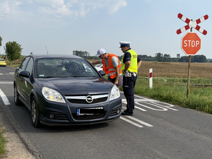 Policjant i przedstawiciel PKP rozmawia z kierowcą i wręcza ulotkę