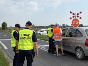 Policjant i przedstawiciel PKP rozmawia z kierowcą, funkcjonariusze SOK stoją