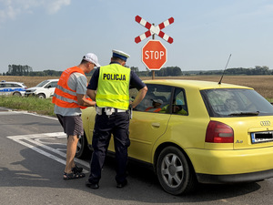 Policjant i przedstawiciel PKP rozmawiają z kierowca i wręczają ulotkę